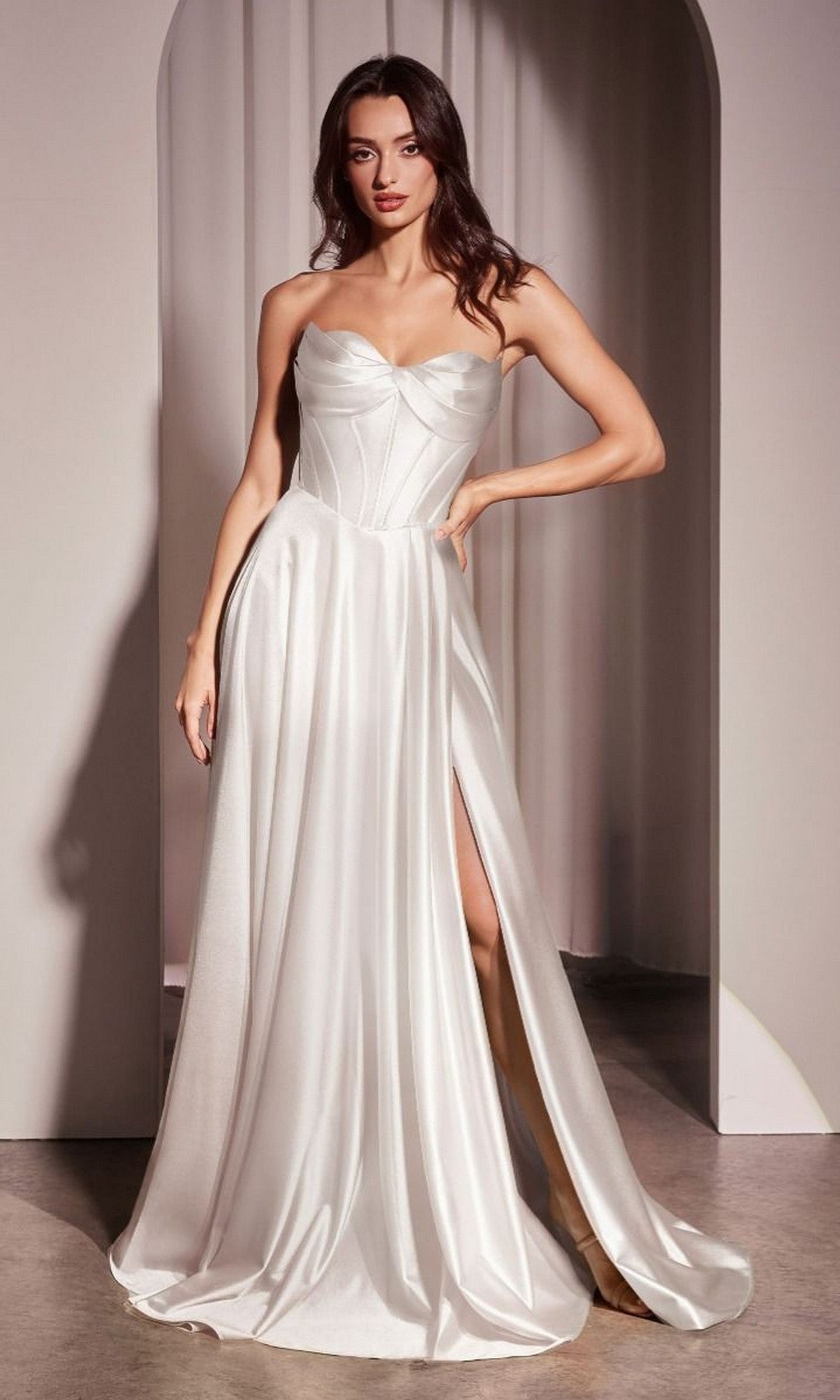 A woman in the Ladivine CD378W white strapless satin wedding gown with a high slit stands before a neutral arched backdrop.
